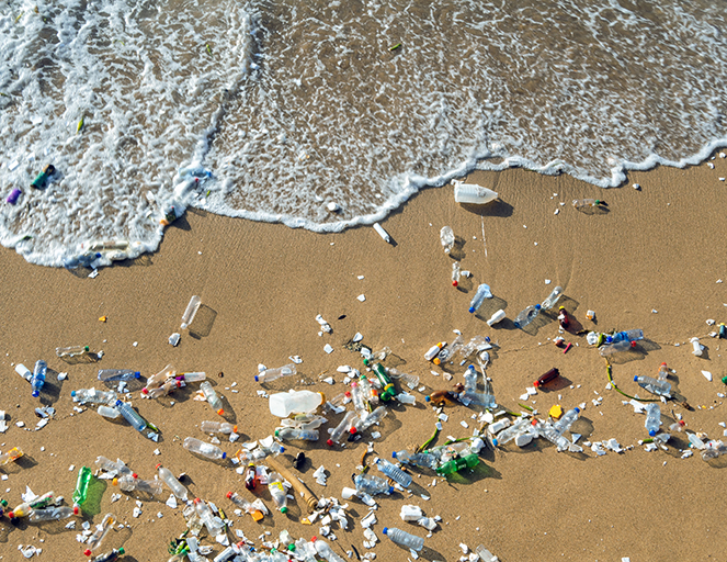 Plastikflaschen und Mikroplastik verteilt am Sandstrand, Wellen spülen Müll ans Ufer