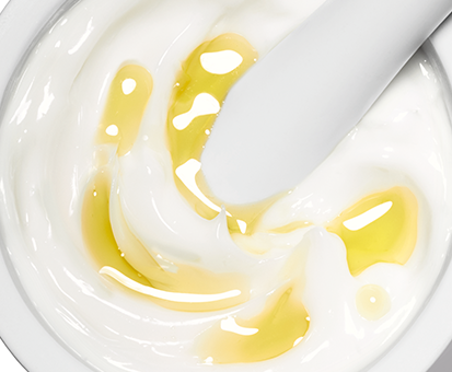 Nahaufnahme von weißer Creme mit goldgelbem Öl, vermischt mit einem weißen Spatel