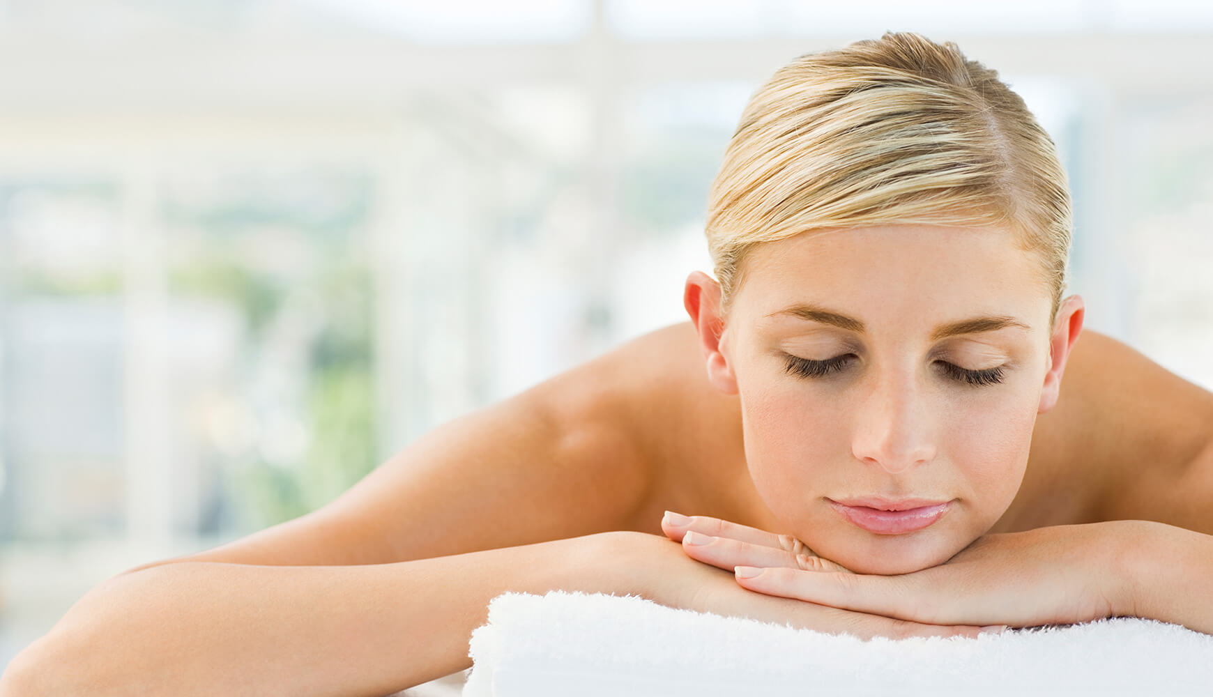 Frau liegt entspannt mit geschlossenen Augen auf weißem Handtuch bei Massage oder Wellnessbehandlung