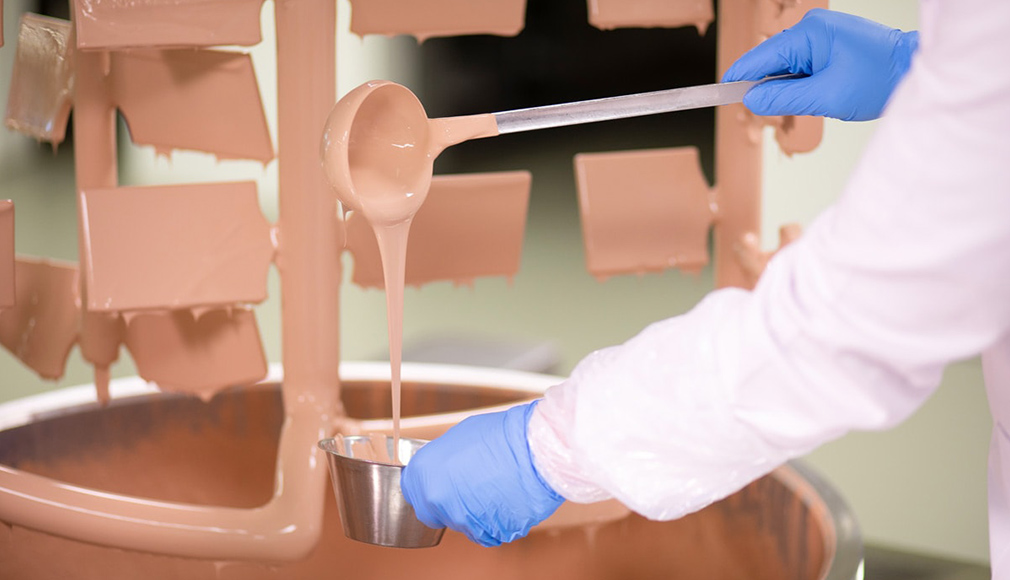 Hersteller gießt flüssige Foundation in Behälter, Hände mit blauen Handschuhen, Produktionsumgebung
