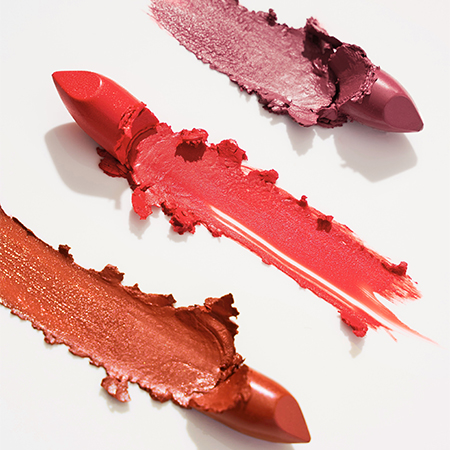 Drei Lippenstifte in Rot, Rosa und Braun mit Farbspuren auf weißem Hintergrund