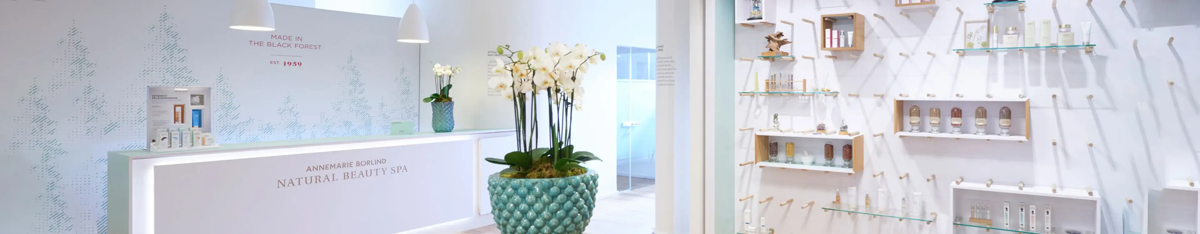 Empfangstresen im ANNEMARIE BÖRLIND Natural Beauty Spa mit weißen Wänden und Produktregalen, Orchideen in Vase