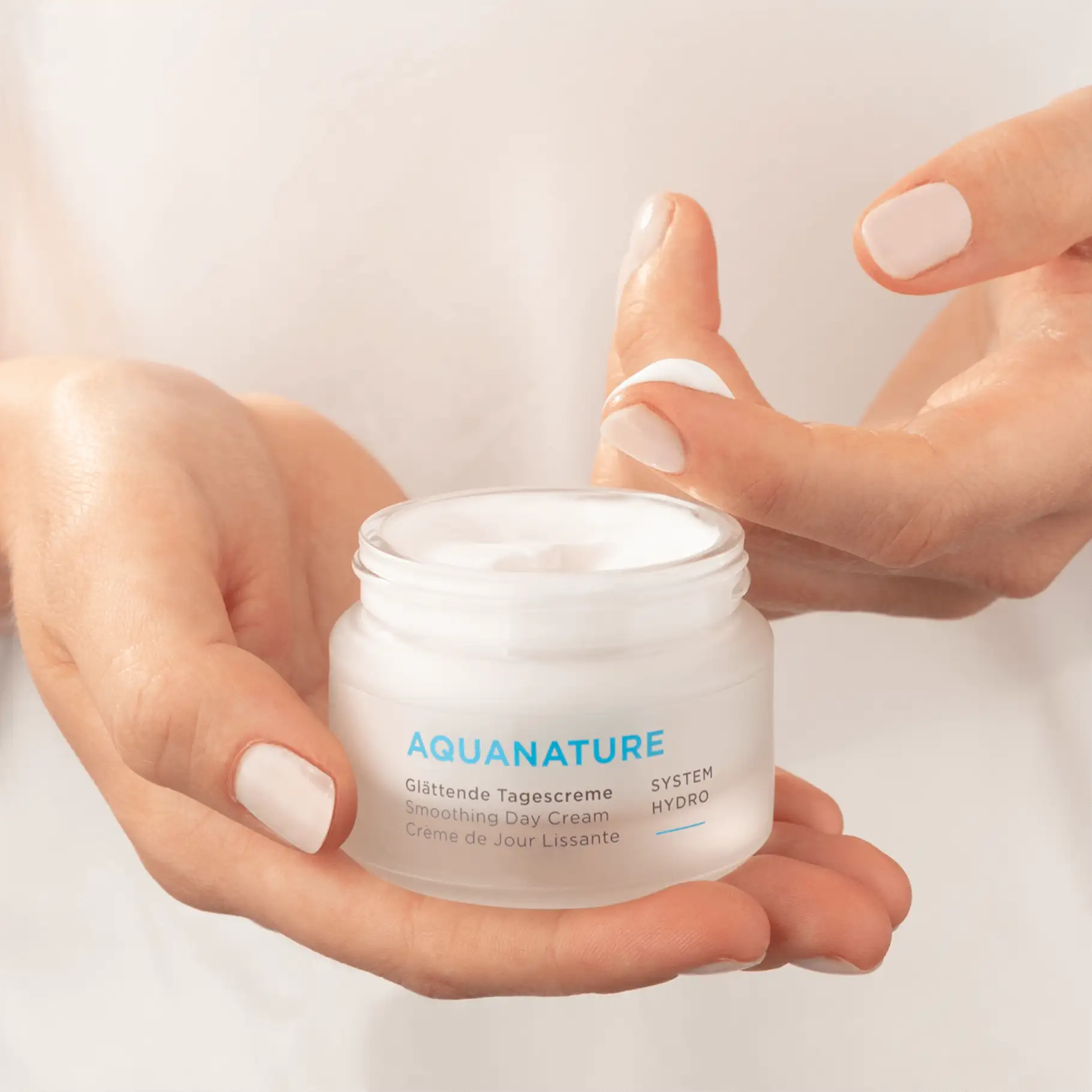 AQUANATURE Glättende Tagescreme im Tiegel, Hand hält Creme, Finger nimmt Produktprobe