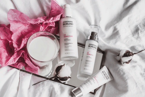 ANNEMARIE BÖRLIND ZZ Sensitive Pflegeserie mit Lotion, Serum und Creme auf weißem Stoff mit Baumwollzweigen