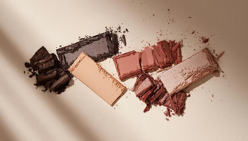 Blaue Augen schminken Zerbrochene Lidschatten in natürlichen Braun-, Rosé- und Beigetönen auf hellem Untergrund – ideal für ein Augen-Make-up bei blauen Augen.