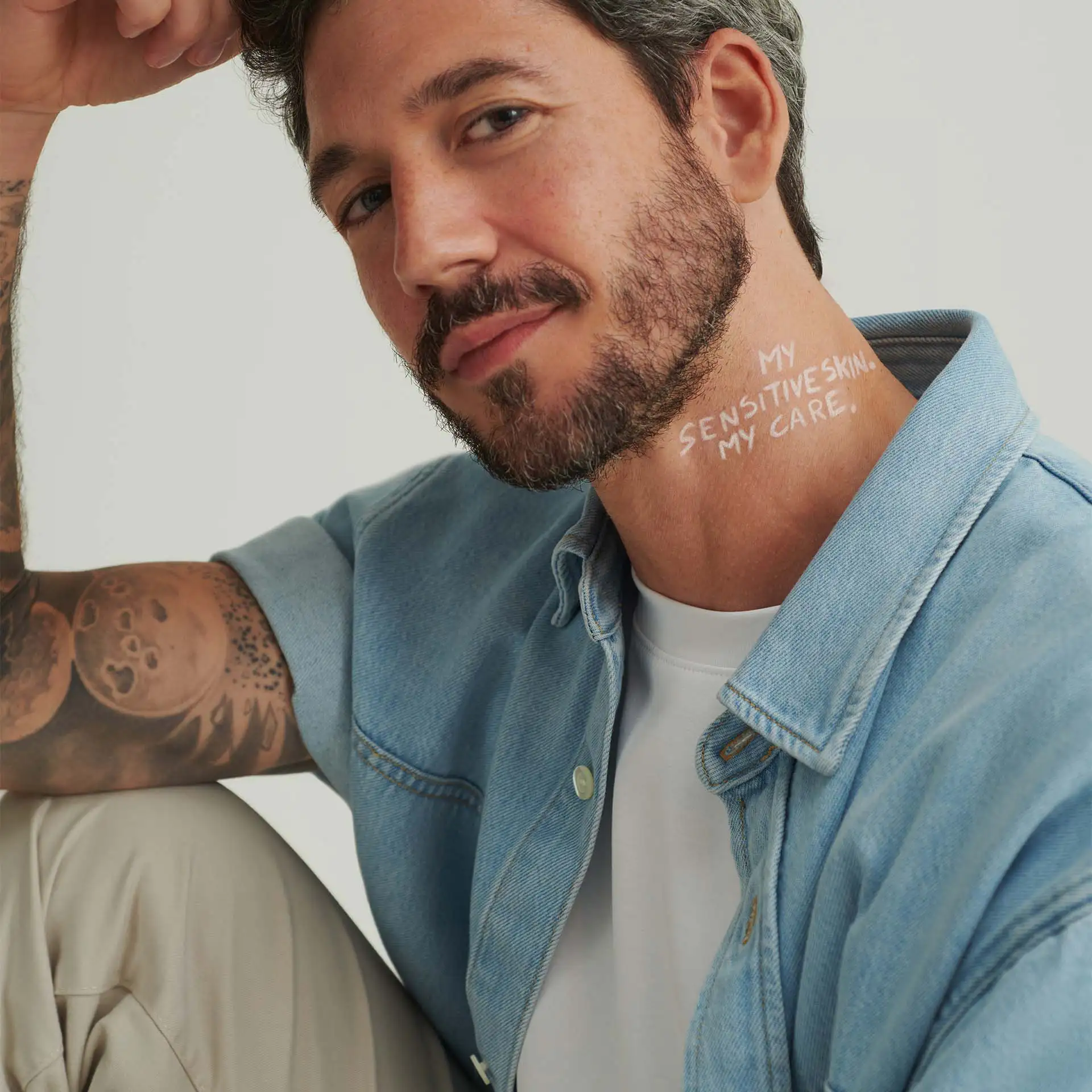 Mann mit Bart und Tattoos trägt hellblaue Jeansjacke, Schriftzug "My sensitive skin, my care." am Hals