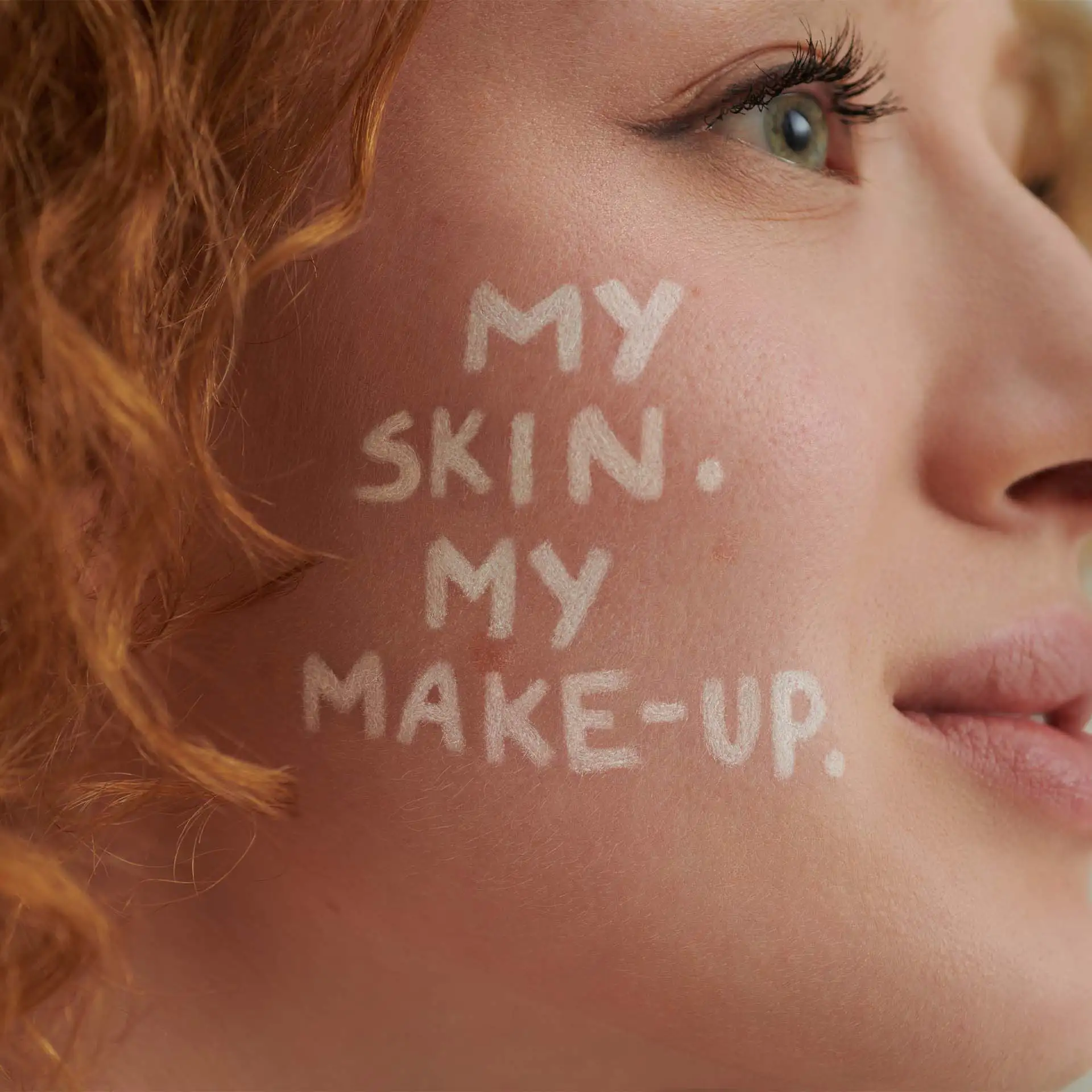 Seitenansicht eines Gesichts mit rotem Haar und dem Text "MY SKIN. MY MAKE-UP." auf der Wange
