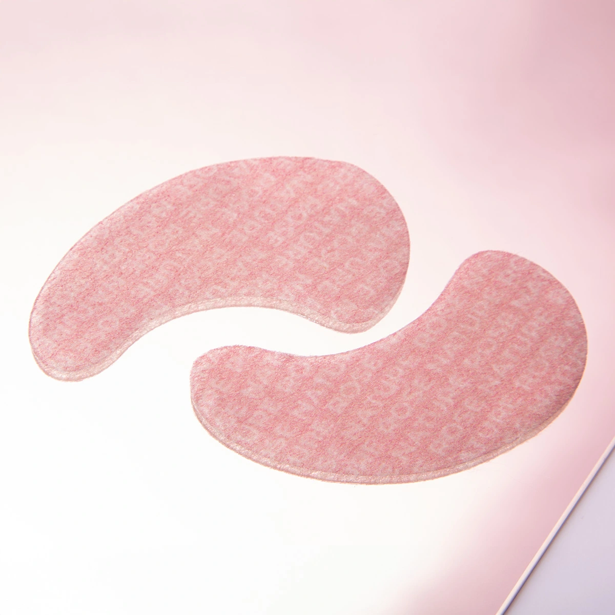 Zwei rosa, gebogene Augenpads mit feiner Textur auf hellem, rosafarbenem Hintergrund
