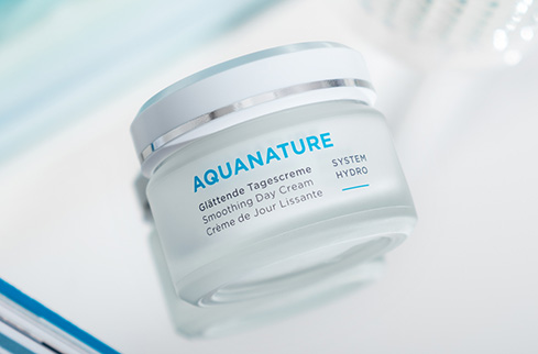 AQUANATURE glättende Tagescreme im weißen Tiegel mit silbernem Deckel auf hellem Hintergrund