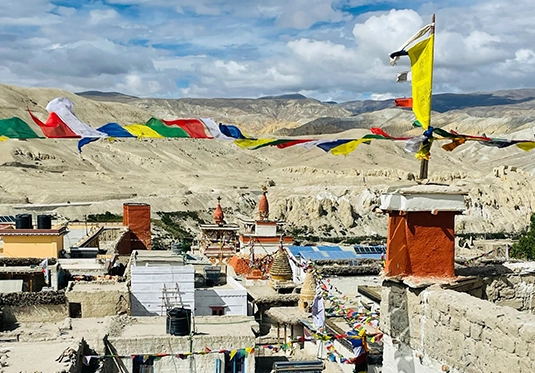 Blick auf das Dorf Lomanthang in Nepal mit bunten Gebetsfahnen und kargen Bergen im Hintergrund