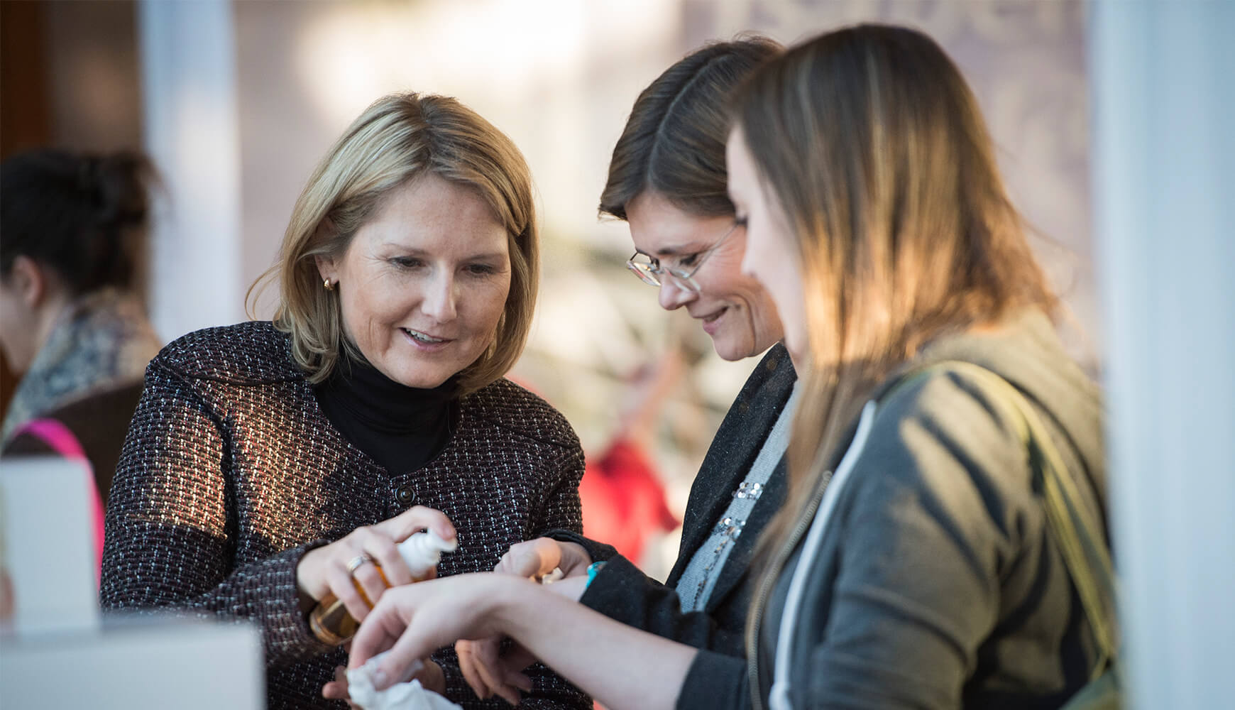 Beratungssituation mit drei Frauen, eine trägt Pflegeprodukt auf die Hand einer anderen auf
