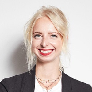 Josephine Rath lächelt in die Kamera, trägt schwarzen Blazer und weiße Bluse vor weißem Hintergrund