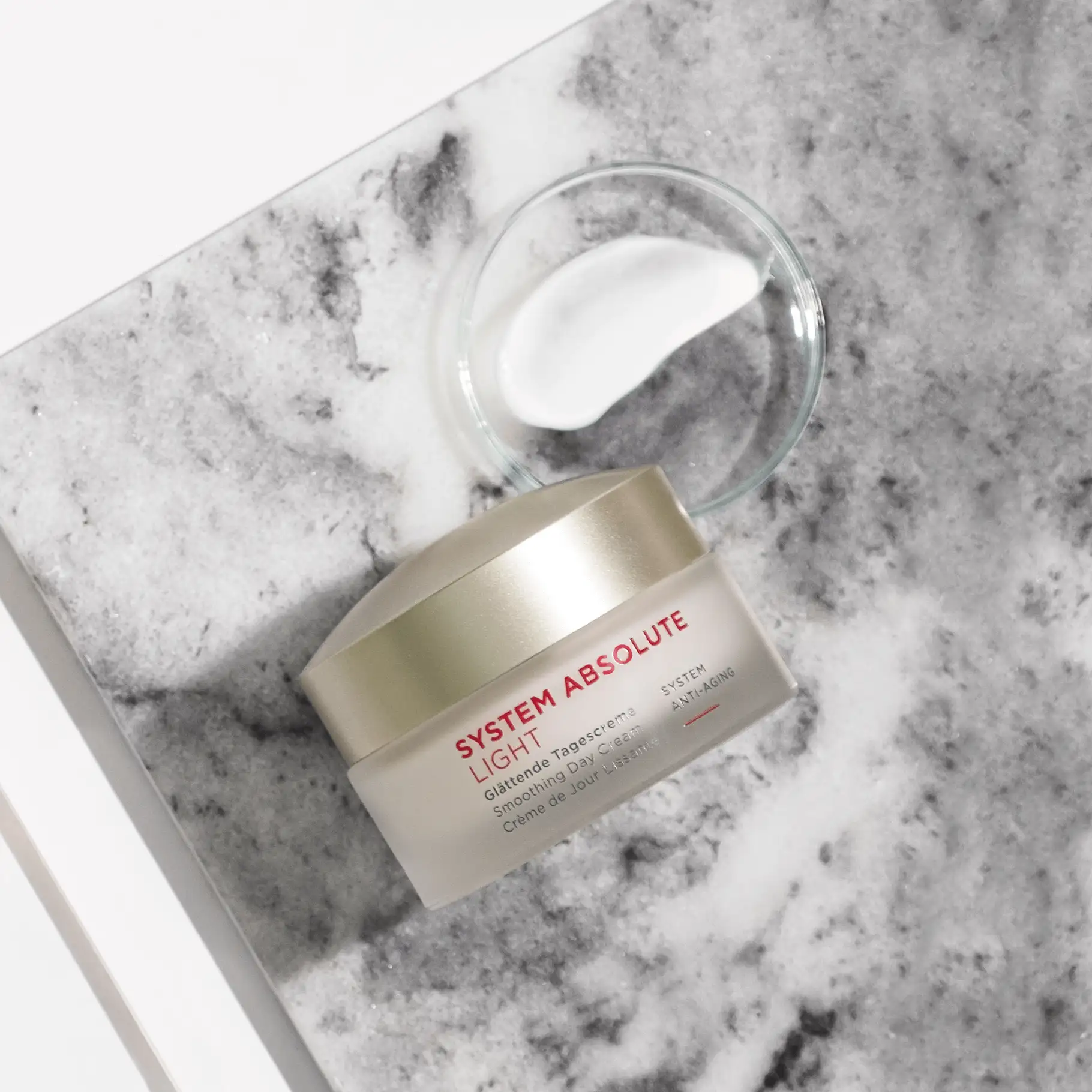 SYSTEM ABSOLUTE LIGHT glättende Tagescreme im Tiegel mit weißer Creme auf grauem Marmorhintergrund