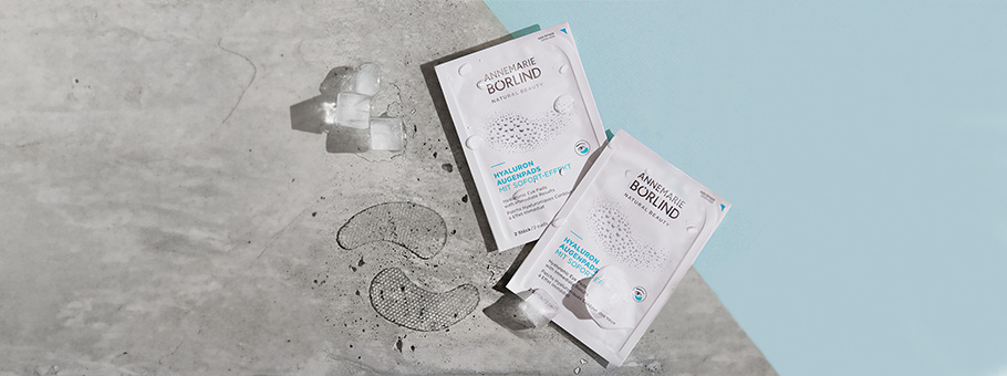 ANNEMARIE BÖRLIND Hyaluron Augenpads mit Sofort-Effekt, zwei Packungen und Eiswürfel auf grauem Untergrund