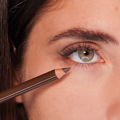 Nahaufnahme eines Auges mit grün-brauner Iris und braunem Kajalstift, der an der unteren Wimpernlinie ansetzt