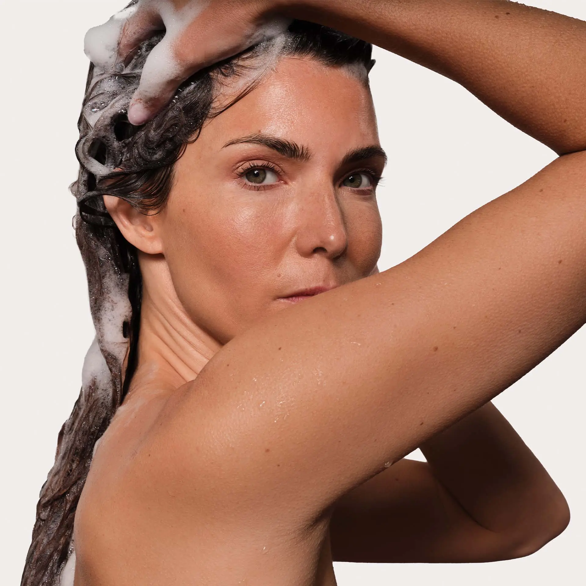 Frau mit nassem Haar, die Shampoo verwendet und auf dem Kopf massiert, Augen offen in entspannter Haltung