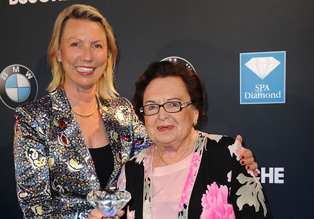 Zwei Frauen vor schwarzem Hintergrund mit BMW- und SPA Diamond-Logo, eine hält einen Kristallglas-Pokal