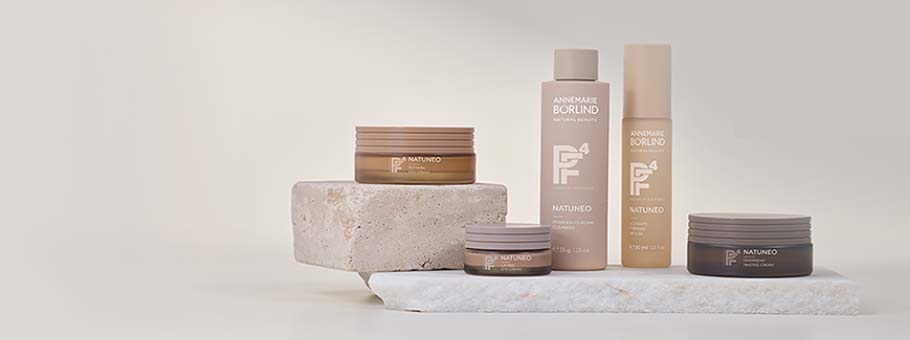 ANNEMARIE BÖRLIND NATUNEO Serie mit Creme, Lotion und Serum in braunen und beigen Verpackungen auf Steinplatten