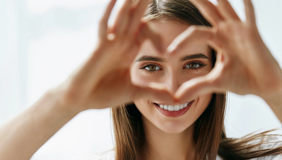 Lachende Frau mit Herzform aus den Händen vor dem Gesicht – natürliches Augen Make-up für den Alltag