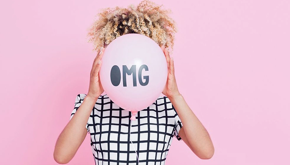 Pickel durch Stress Person hält rosa Ballon mit schwarzem Schriftzug "OMG" vor ihr Gesicht vor einfarbig rosa Hintergrund