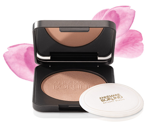 ANNEMARIE BÖRLIND Bronzing Puder in schwarzer Dose mit Spiegel und weißem Applikator vor rosa Blütenblatt-Hintergrund