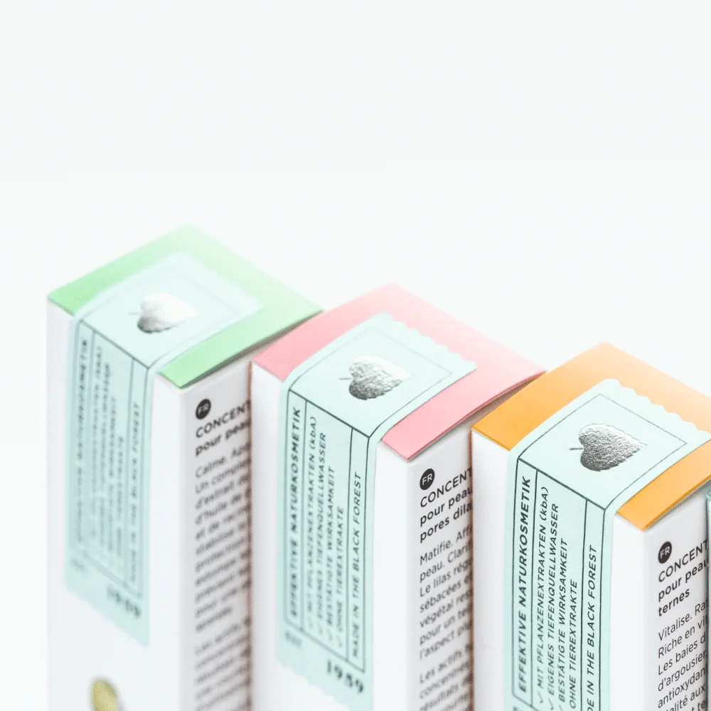 Drei Produktverpackungen mit pastellfarbenen Deckeln in Grün, Rosa und Orange, Naturkosmetik mit Silberherz-Label