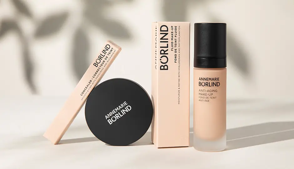 Nachhaltige Make-up-Produkte und Faltschachteln von ANNEMARIE BÖRLIND vor neutralem Hintergrund mit sanften Blattschatten.