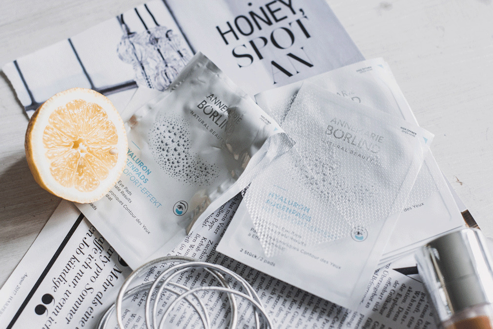 ANNEMARIE BÖRLIND Hyaluron Augenpads auf Zeitungen mit Zitronenhälfte und Kopfhörerkabel