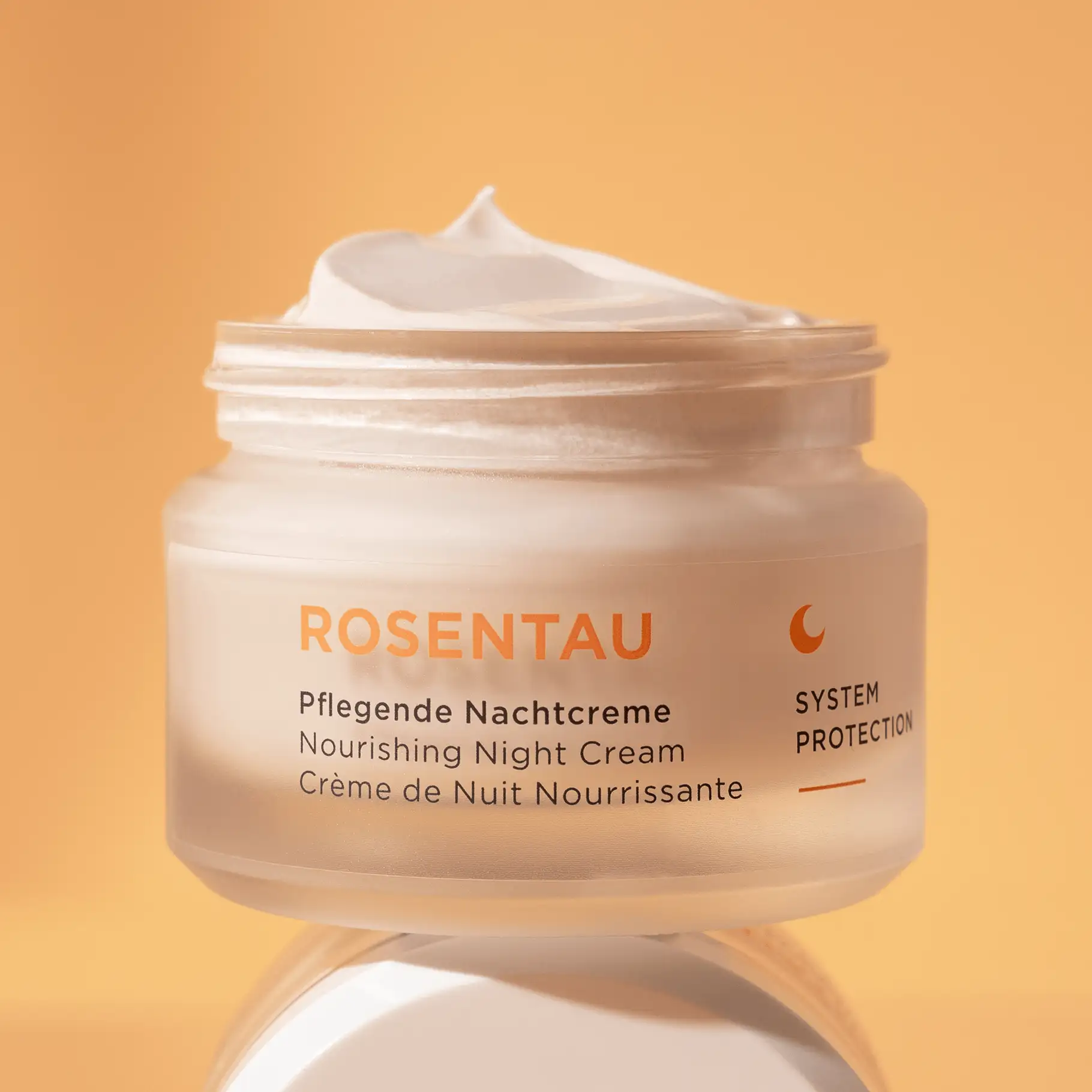 ROSENTAU pflegende Nachtcreme im geöffneten Tiegel mit cremiger Textur vor orangefarbenem Hintergrund