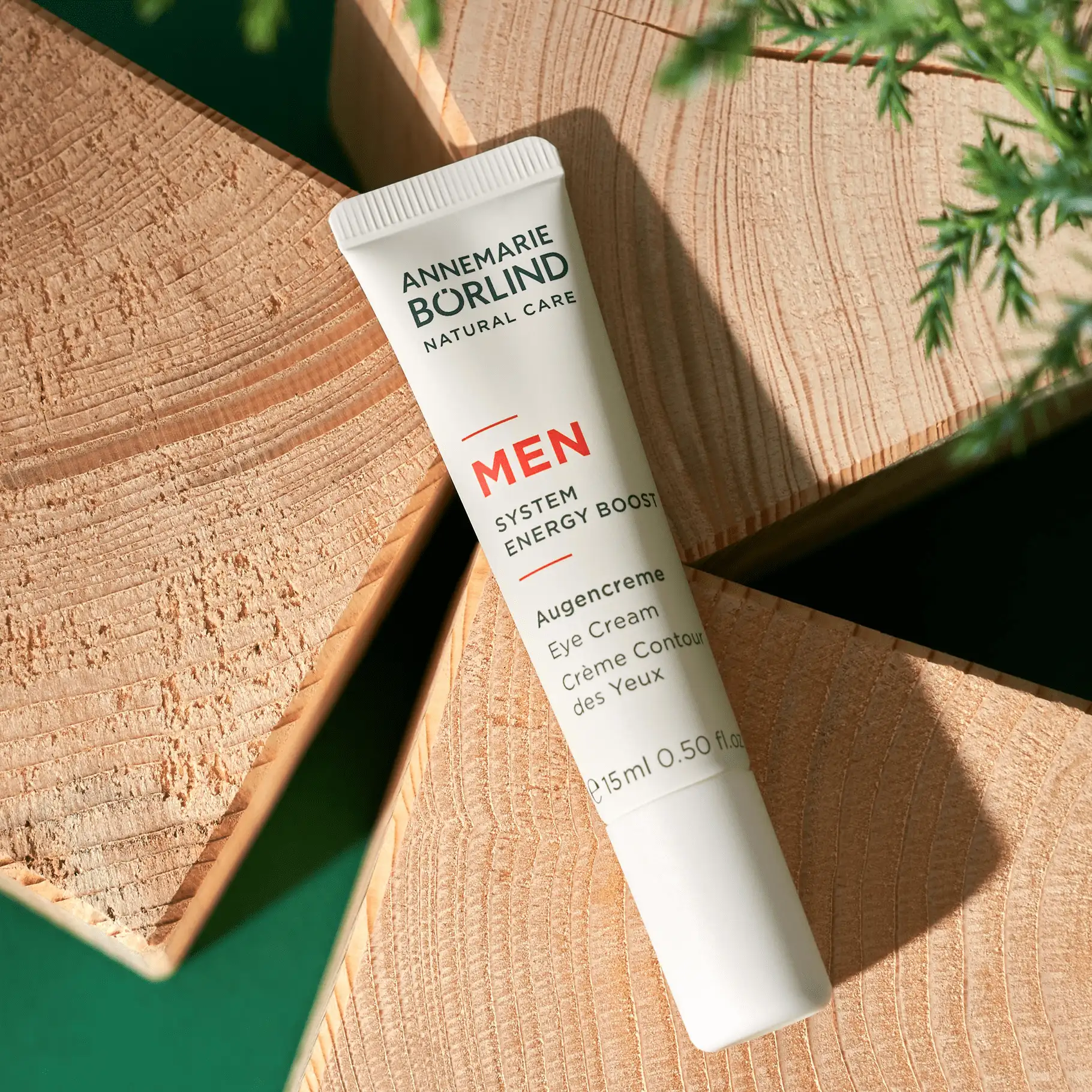 ANNEMARIE BÖRLIND MEN Augencreme Tube auf Holzflächen mit grünen Pflanzenelementen im Hintergrund