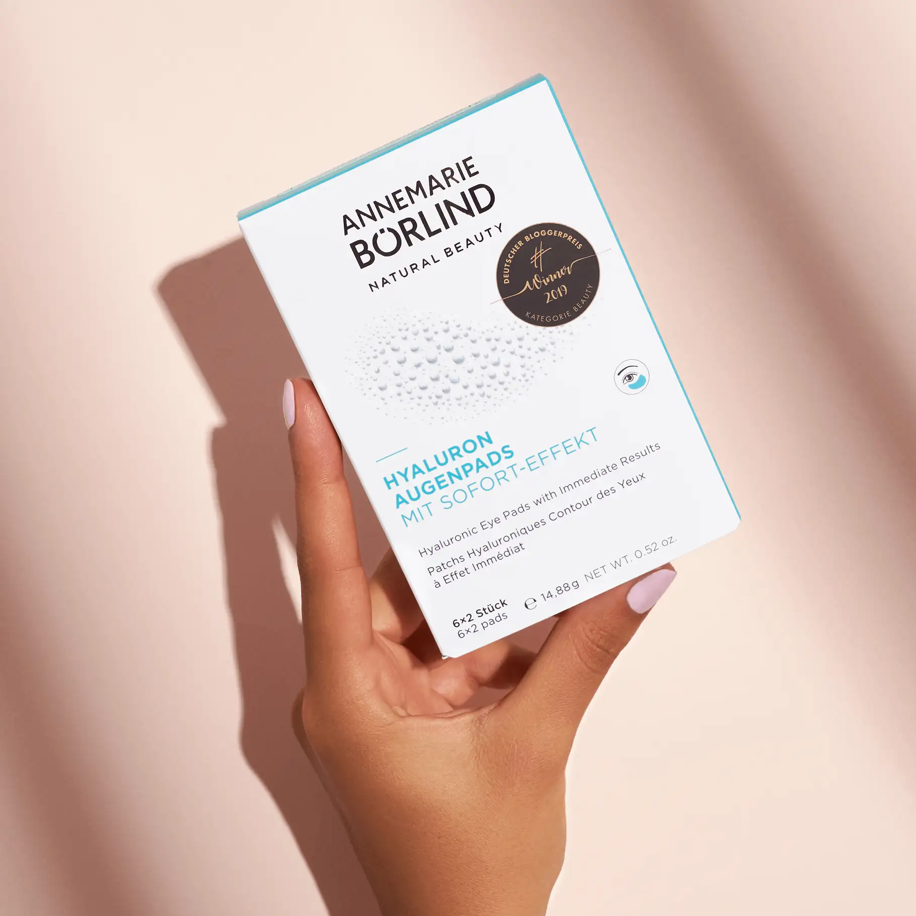 Hand hält ANNEMARIE BÖRLIND Hyaluron Augenpads Faltschachtel mit Sofort-Effekt vor hellem Hintergrund