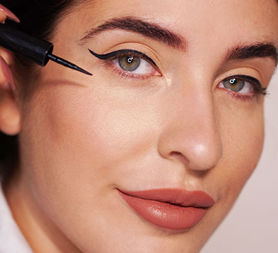 Nahaufnahme einer Frau, die mit einem Eyeliner einen präzisen Lidstrich an einem mandelförmigen Auge zieht