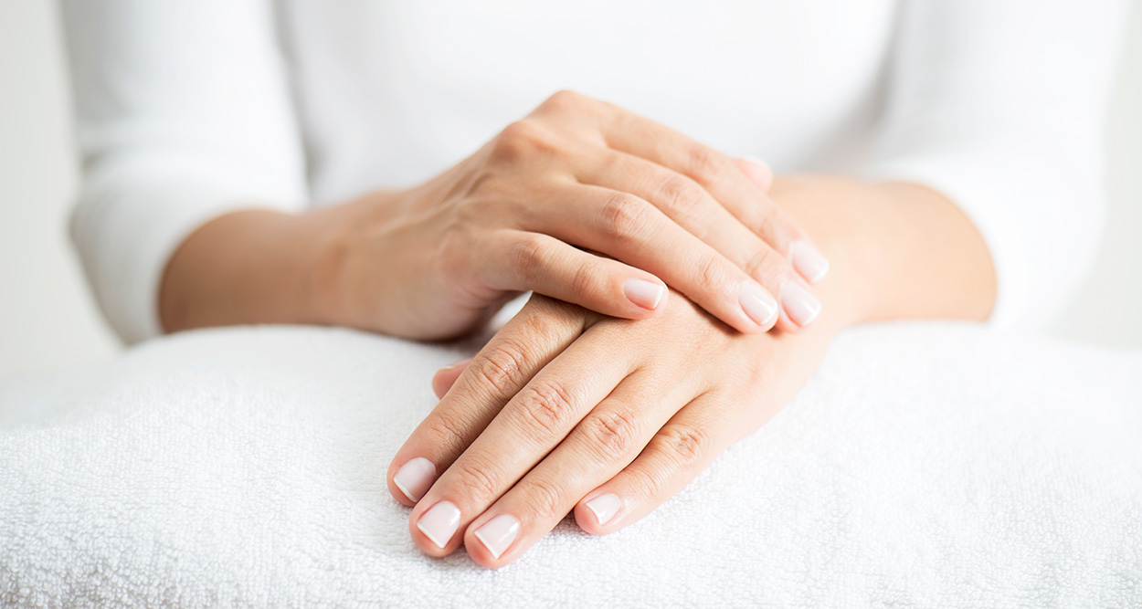 Zwei Hände liegen entspannt auf einem weißen Handtuch, gepflegte Nägel und glatte Haut sichtbar