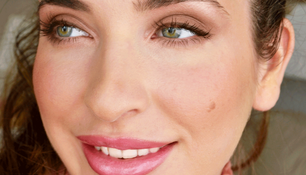 Nahaufnahme eines lächelnden Gesichts mit grünlichen Augen, dezentem Make-up und natürlichem Licht