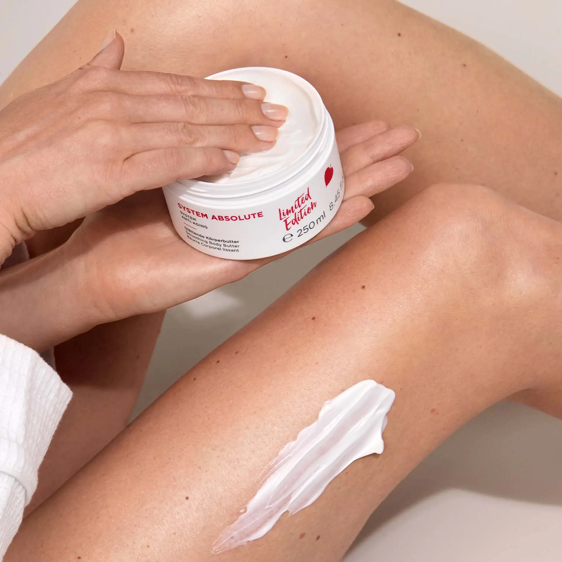 Frau trägt SYSTEM ABSOLUTE Glättende Körperbutter auf Bein auf