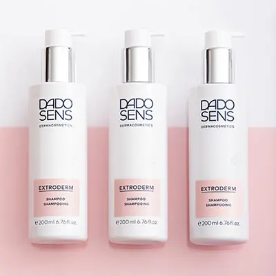 DADO SENS EXTRODERM Shampoo gegen schuppige Kopfhaut, 3 weiße Flaschen à 200 ml auf rosa Untergrund