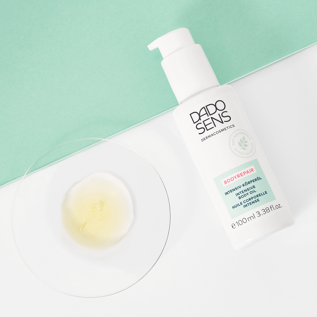DADO SENS BODYREPAIR Intensiv-Körperöl in weißer Flasche mit Pumpspender und Ölprobe auf Glasplatte
