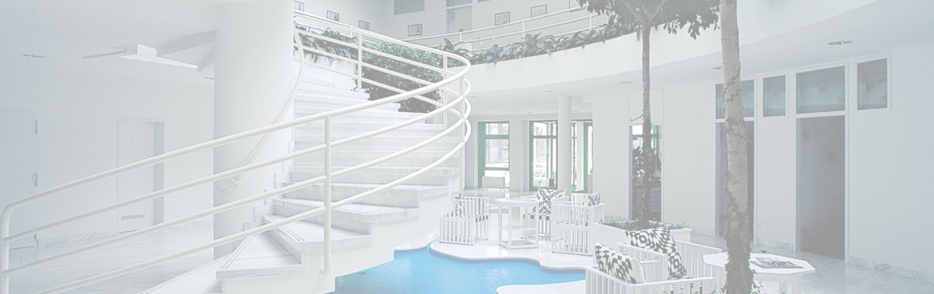 Helles Foyer mit geschwungener Treppe, Sitzgruppen mit gemusterten Kissen und Innenbäumen