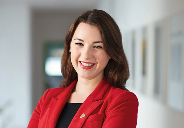 Frau in rotem Blazer lächelt selbstbewusst in einem hellen Büroflur mit unscharfem Hintergrund