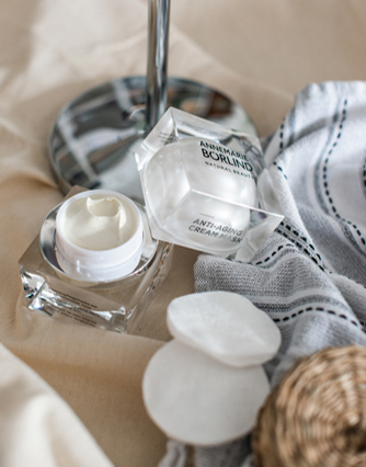ANNEMARIE BÖRLIND Anti-Aging Cream M SPF 15 in offenem Tiegel mit Wattepads und Handtuch auf beige Oberfläche