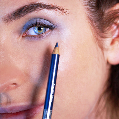 Nahaufnahme einer Frau mit blauem Lidschatten, die einen blauen Kajalstift an die untere Augenlinie hält