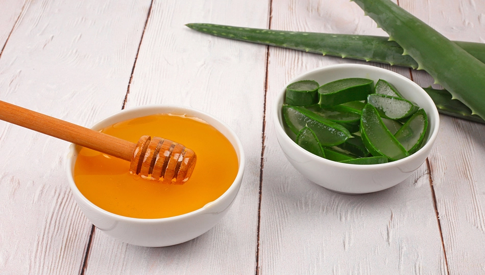 Natürliche Hausmittel gegen trockene und spröde Lippen Honig in weißer Schale mit Holzlöffel und geschnittene Aloe Vera Blätter in zweiter Schale auf Holzuntergrund