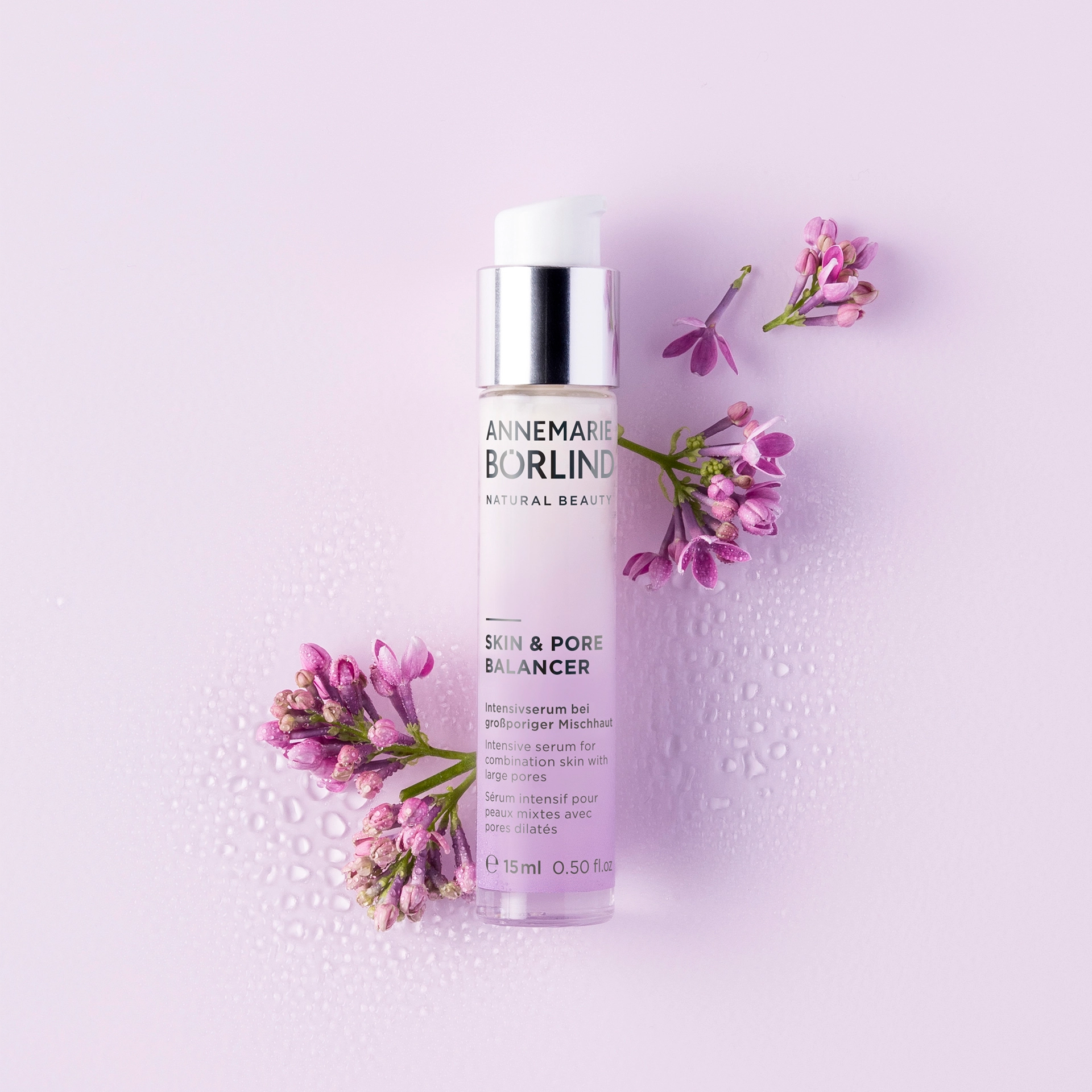ANNEMARIE BÖRLIND Skin & Pore Balancer Serum mit Pumpspender, umgeben von lila Blüten auf hellem Hintergrund