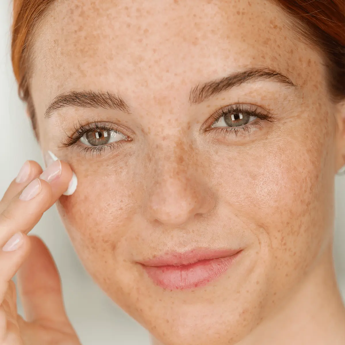 Frau trägt sanft Creme auf die Wange auf, Nahaufnahme mit Sommersprossen und natürlichem Hautbild