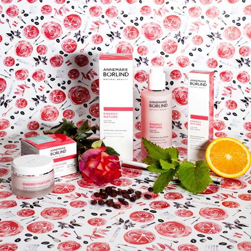 ANNEMARIE BÖRLIND ENERGY NATURE Pflegeprodukte mit Orangen, Minze und Kaffeebohnen vor floralem Hintergrund