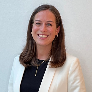 Frau in weißem Blazer und schwarzem Shirt lächelt freundlich vor hellem Hintergrund