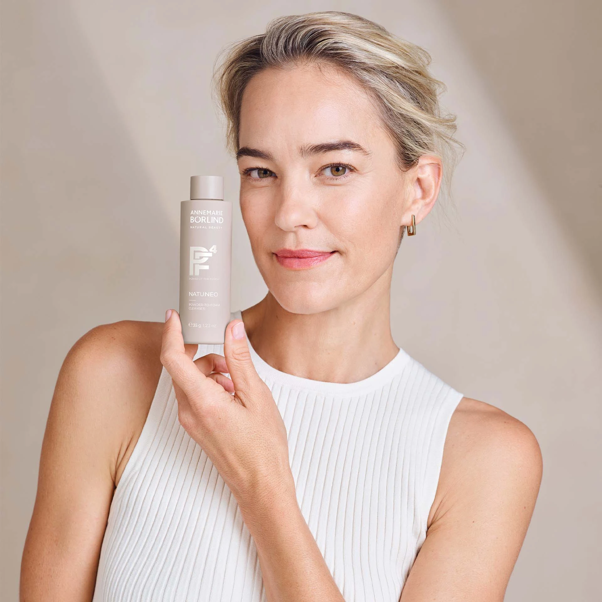 Frau hält ANNEMARIE BÖRLIND NATUNEO Powder-to-Foam Cleanser vor hellem Hintergrund