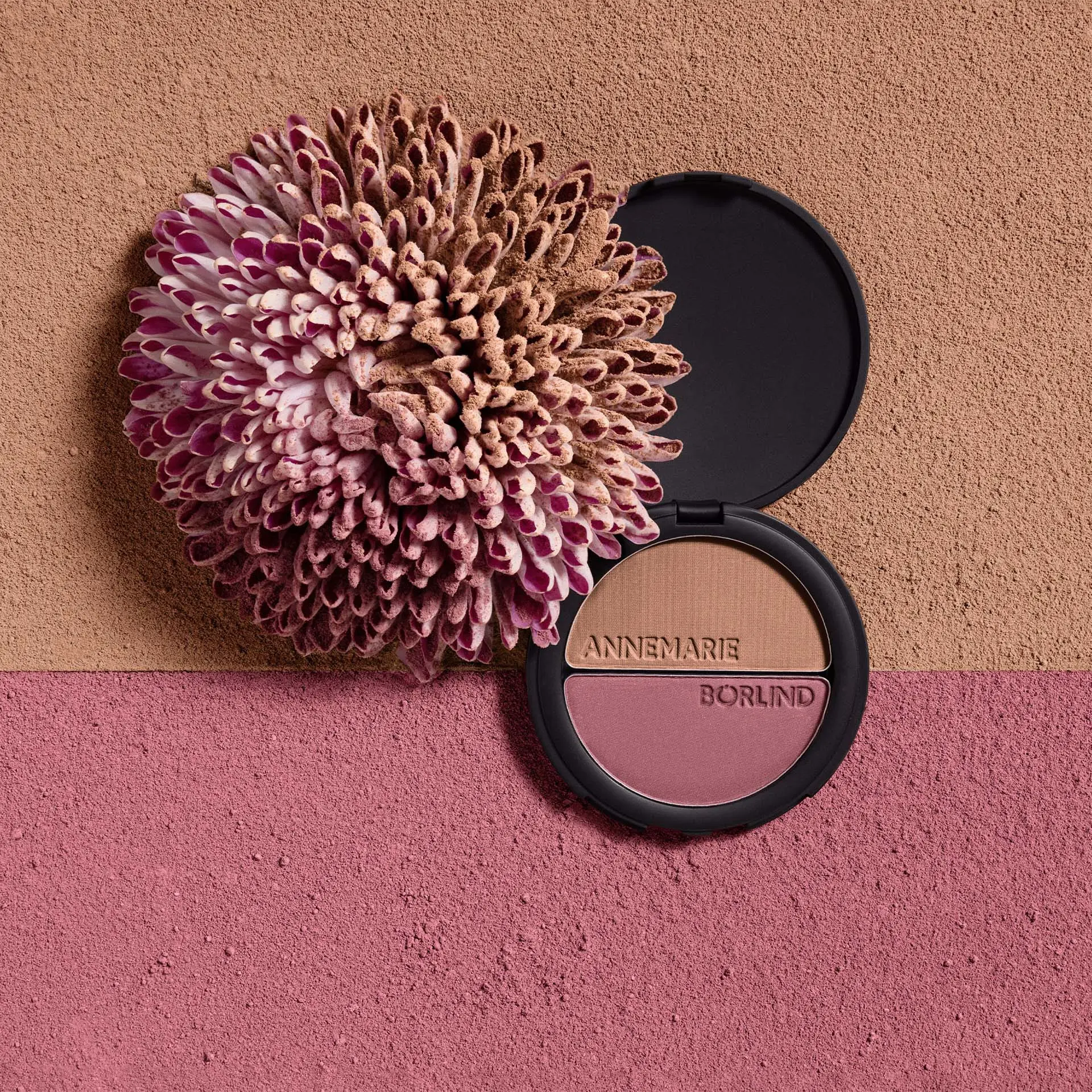 ANNEMARIE BÖRLIND Make-up Duo mit Bronzer und Rouge in schwarzer runder Dose neben Blume vor Hintergrund mit Textur