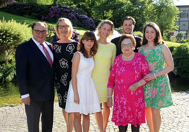 Sieben Personen in sommerlicher Kleidung stehen im Garten, lächeln in die Kamera, sonniger Tag