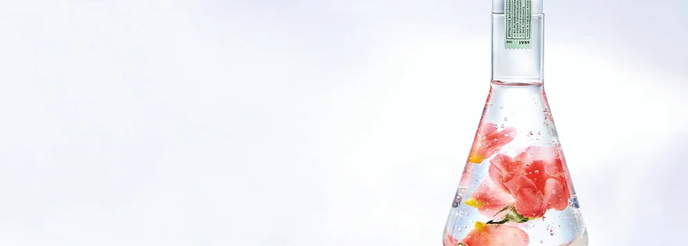 Flasche mit klarem Flüssigkeitsgel und eingetauchten rosa Rosenblüten vor weißem Hintergrund